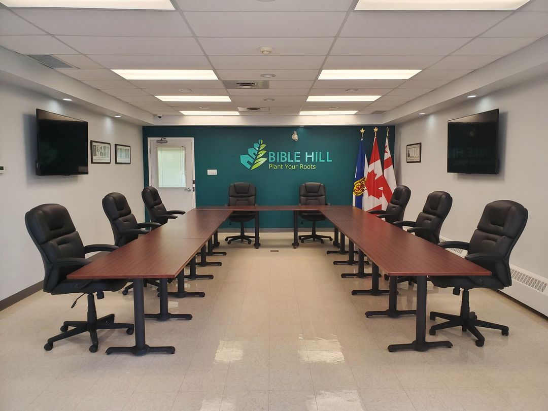 8 black chairs seated around a U shaped boardroom table, in the Bible Hill Commission Chambers, with 3 flag in the corner of the room (Nova Scotia, Canada and Grand Council)